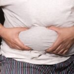 A close-up view of a man holding his tummy while sitting on a couch, highlighting lifestyle choices.