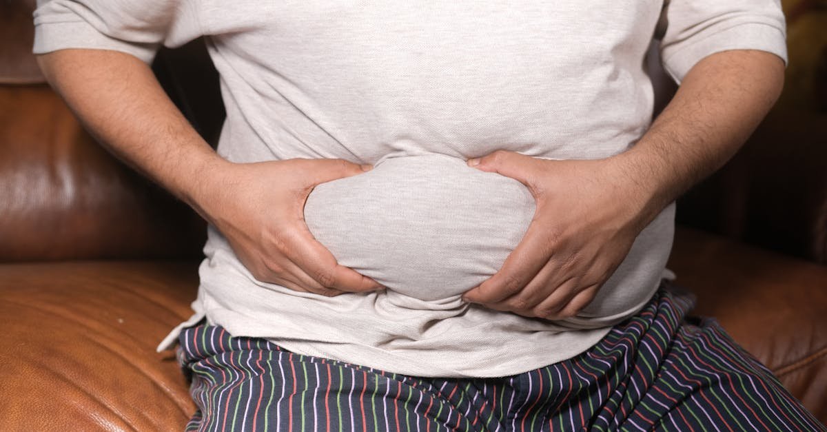 A close-up view of a man holding his tummy while sitting on a couch, highlighting lifestyle choices.