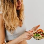 A caucasian woman in a sports bra enjoying a fresh salad, embodying healthy eating and lifestyle.