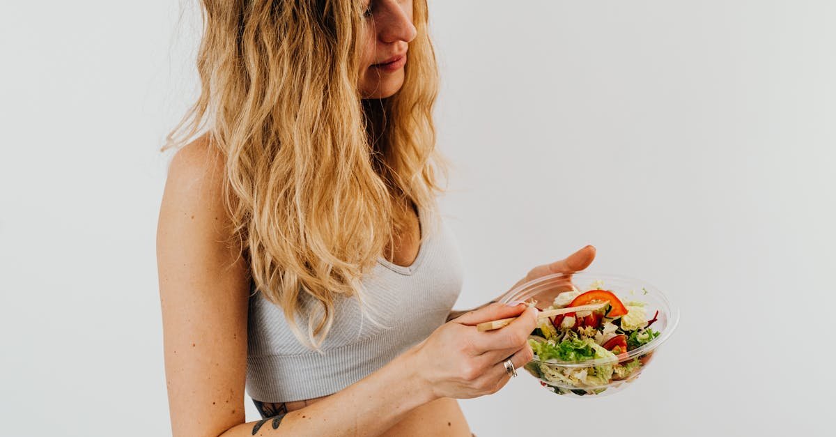 A caucasian woman in a sports bra enjoying a fresh salad, embodying healthy eating and lifestyle.