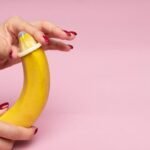 Close-up of hands demonstrating condom application on a banana, symbolizing safe sex education.