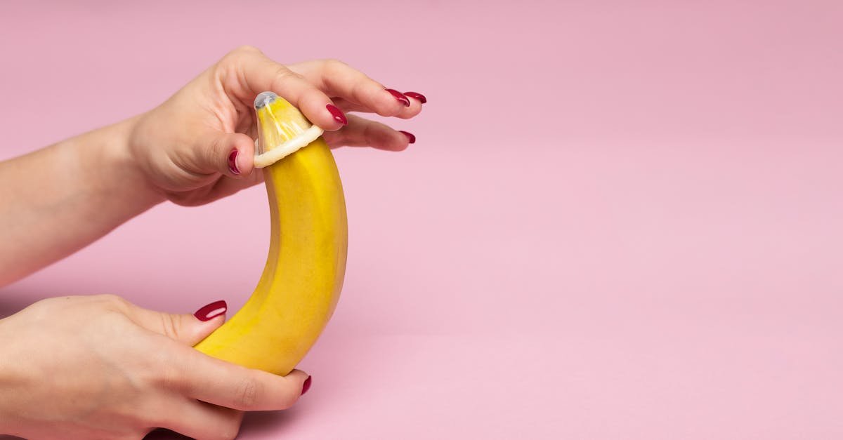 Close-up of hands demonstrating condom application on a banana, symbolizing safe sex education.