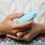 Close-up of hands holding a blue personal massager against a knitted sweater.
