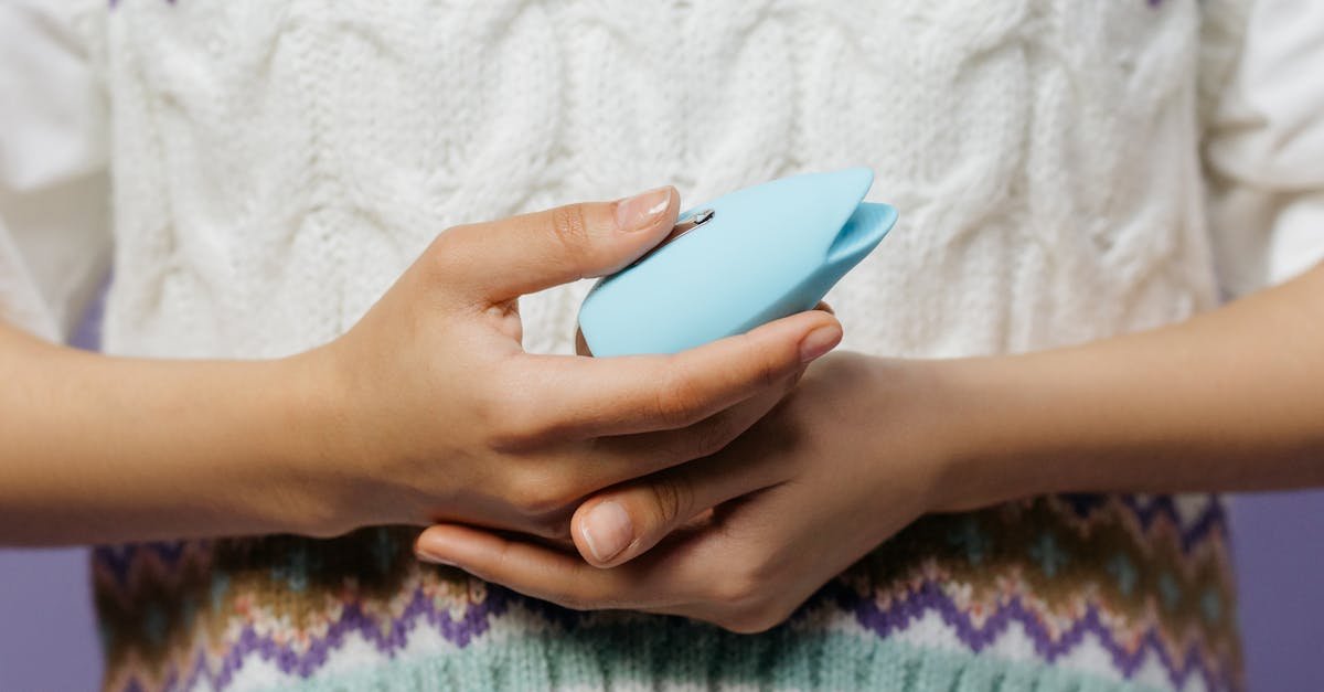 Close-up of hands holding a blue personal massager against a knitted sweater.