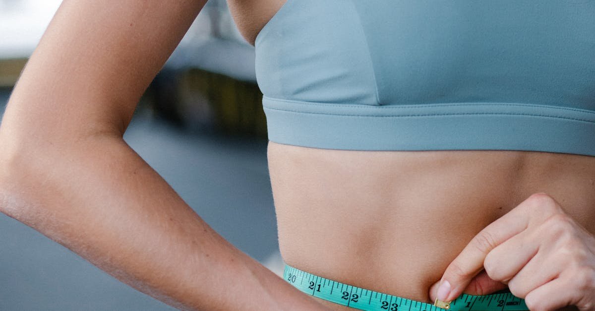 Female athlete measuring waistline with tape for health tracking in gym.