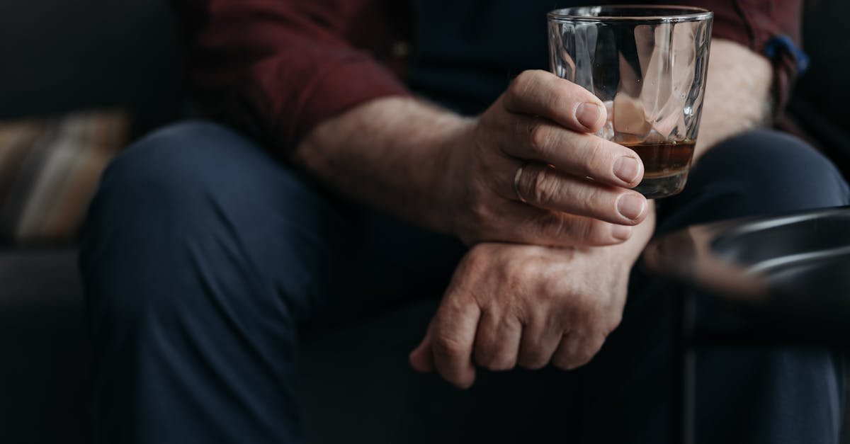 A detailed image of an adult hand holding a whiskey glass indoors.
