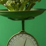 Fresh broccoli displayed on a vintage green weighing scale against a green background.