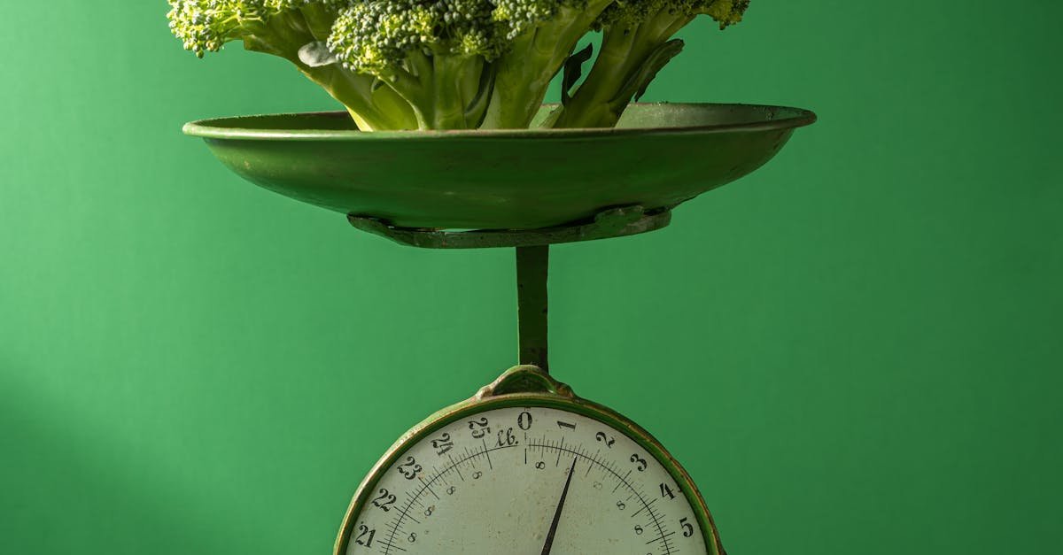 Fresh broccoli displayed on a vintage green weighing scale against a green background.