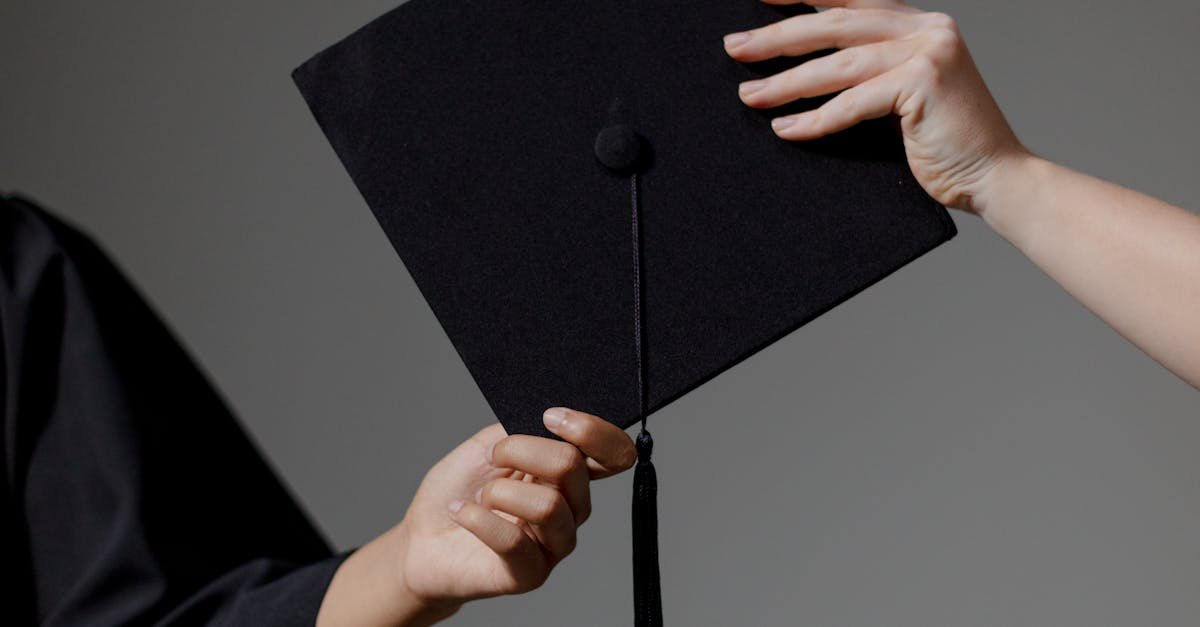 Two people exchanging a graduation cap on a grey background, symbolizing achievement.